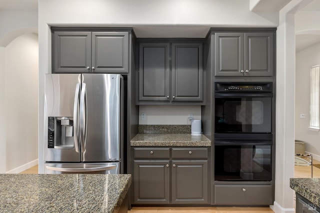 kitchen with stainless steel fridge with ice dispenser, black double oven, and dark stone counters