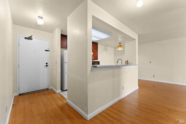 kitchen with refrigerator, sink, hanging light fixtures, kitchen peninsula, and light wood-type flooring