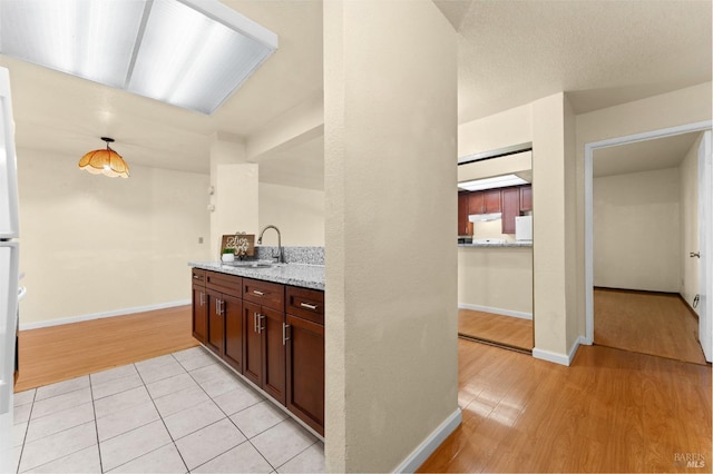 kitchen featuring pendant lighting, light stone countertops, sink, and light wood-type flooring