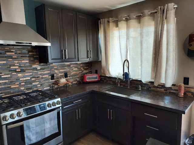 kitchen featuring wall chimney range hood, sink, decorative backsplash, dark stone countertops, and stainless steel range