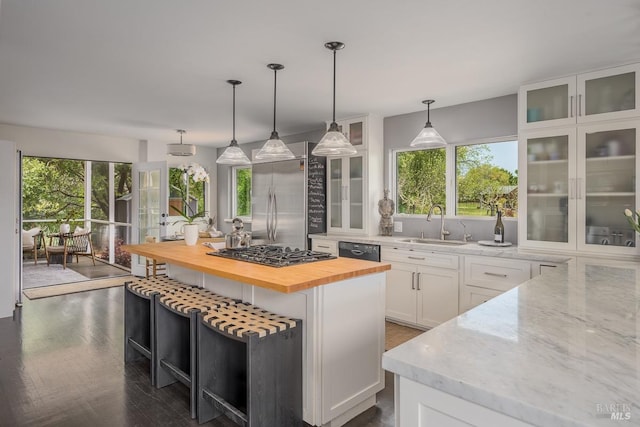 kitchen with stainless steel appliances, sink, white cabinets, a center island, and butcher block counters