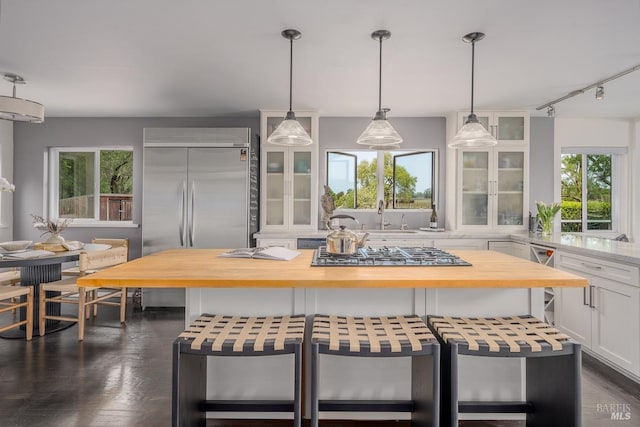 kitchen featuring hanging light fixtures, stainless steel appliances, wood counters, white cabinets, and a kitchen island