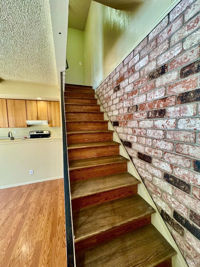 stairs featuring brick wall and wood finished floors