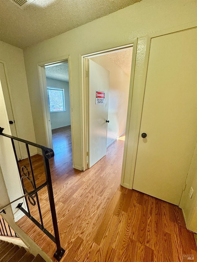 hallway featuring light wood-type flooring and a textured ceiling