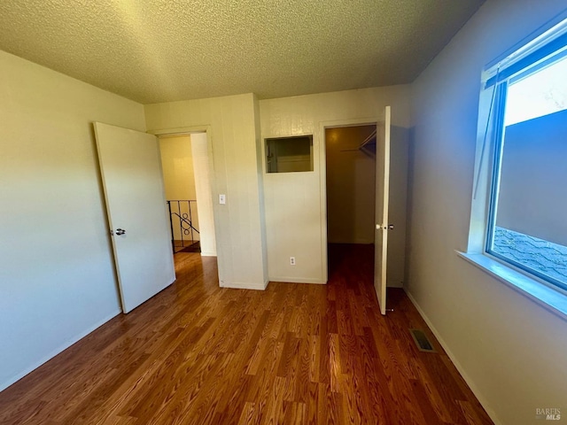 unfurnished bedroom with a textured ceiling, multiple windows, wood finished floors, and visible vents