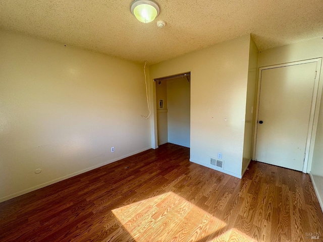 unfurnished bedroom featuring a textured ceiling, wood finished floors, visible vents, baseboards, and a closet