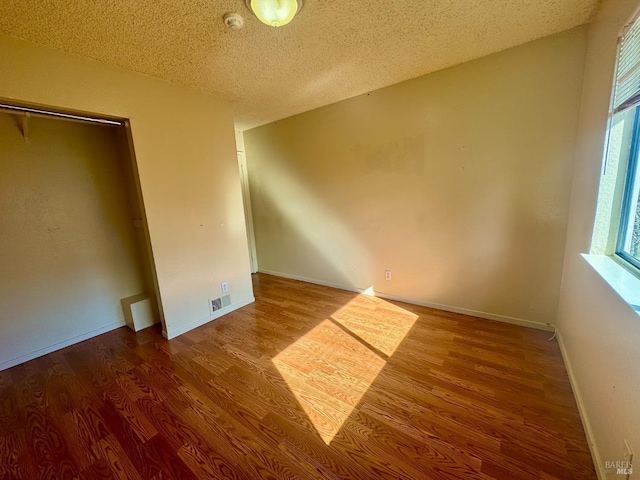 unfurnished bedroom with baseboards, a textured ceiling, visible vents, and wood finished floors