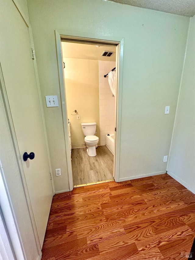 full bath with a textured ceiling, toilet, wood finished floors, visible vents, and shower / bath combination with curtain