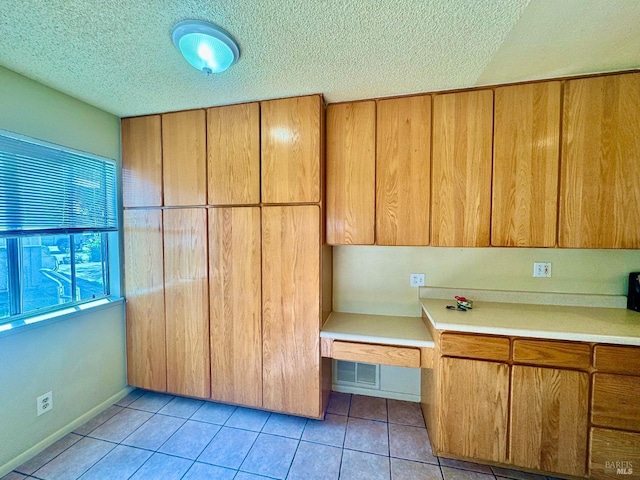 kitchen with light tile patterned floors, visible vents, brown cabinetry, light countertops, and a textured ceiling