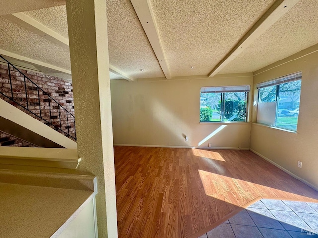 unfurnished room with stairs, a textured ceiling, baseboards, and wood finished floors