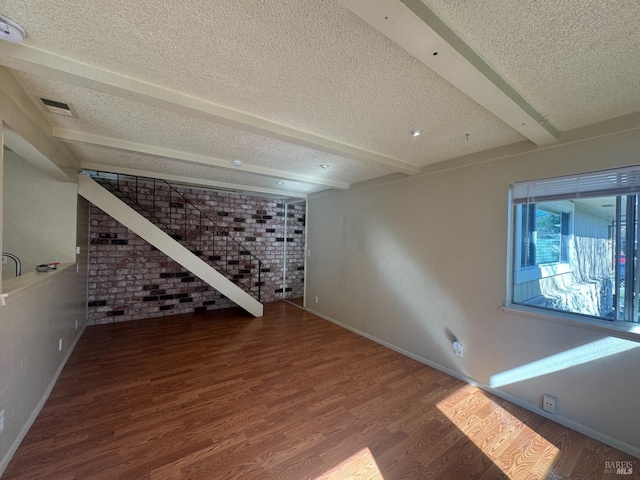 interior space with a textured ceiling, brick wall, wood finished floors, visible vents, and baseboards