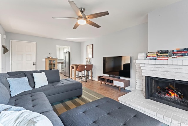 living room featuring ceiling fan, wood-type flooring, and a brick fireplace