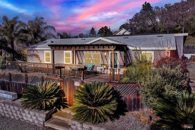 back house at dusk featuring a wooden deck and a pergola