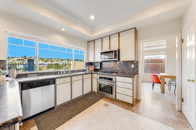 kitchen with sink, a raised ceiling, crown molding, light tile patterned floors, and appliances with stainless steel finishes