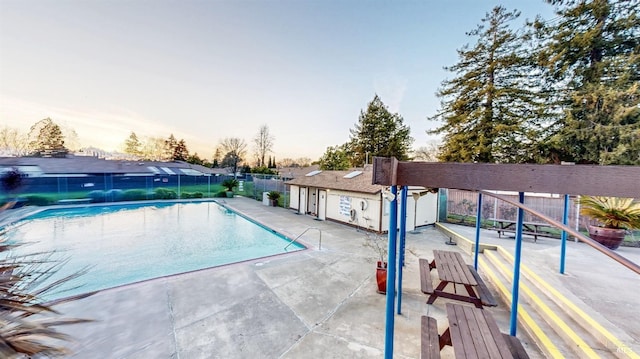 pool at dusk featuring a patio area, a community pool, an outbuilding, and fence