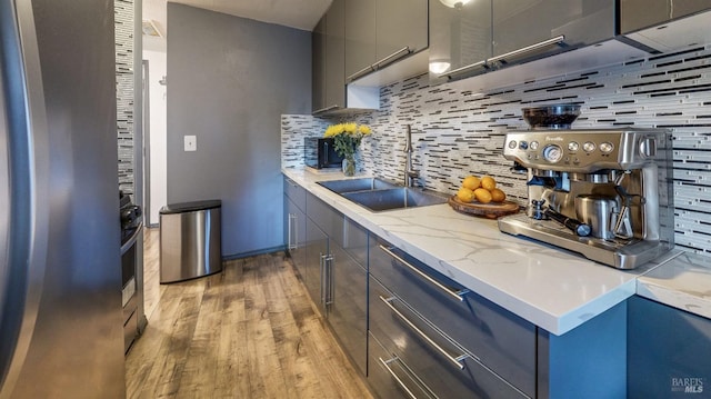 kitchen with light stone countertops, a sink, decorative backsplash, light wood-style floors, and modern cabinets