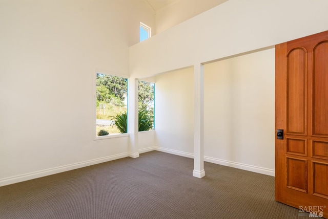 spare room featuring a towering ceiling and dark colored carpet