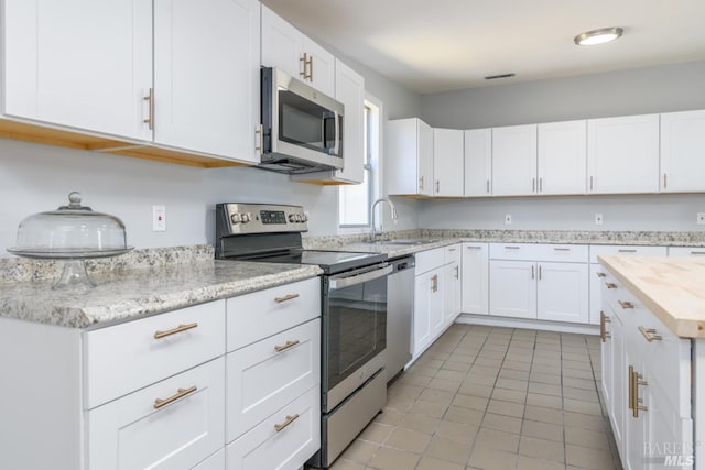 kitchen featuring sink, white cabinetry, appliances with stainless steel finishes, light tile patterned flooring, and butcher block counters