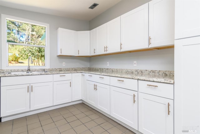 kitchen with white cabinets, light tile patterned floors, light stone counters, and sink