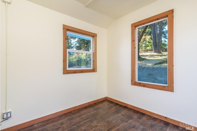 spare room featuring lofted ceiling, dark wood-type flooring, and a healthy amount of sunlight