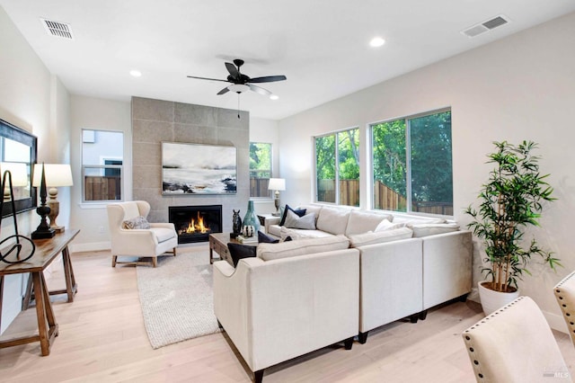 living room featuring a tile fireplace, ceiling fan, and light hardwood / wood-style flooring