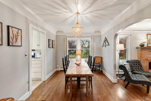 dining room featuring baseboard heating, crown molding, a notable chandelier, a fireplace, and hardwood / wood-style floors