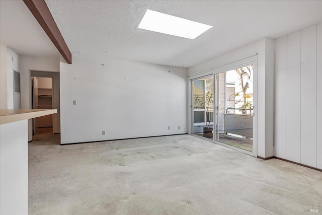 carpeted spare room featuring a textured ceiling, a skylight, and beamed ceiling