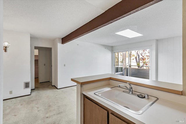 kitchen with sink, light carpet, beamed ceiling, and a textured ceiling