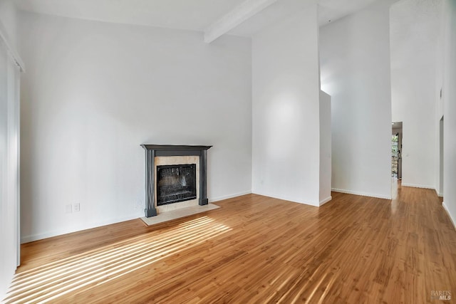 unfurnished living room featuring beam ceiling, a high end fireplace, and light hardwood / wood-style flooring