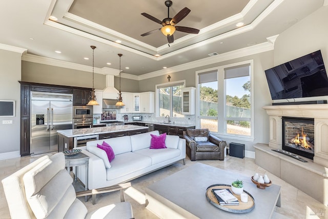 living room with a tray ceiling, ceiling fan, crown molding, and sink