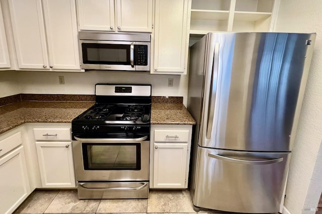 kitchen featuring white cabinets, light tile patterned floors, stainless steel appliances, and dark stone countertops