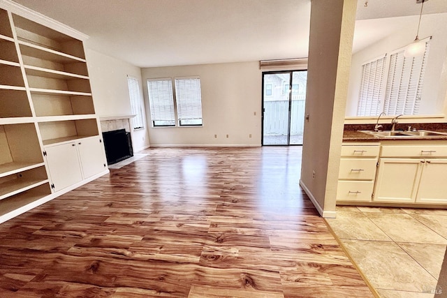 unfurnished living room featuring a tile fireplace, light wood-type flooring, and sink