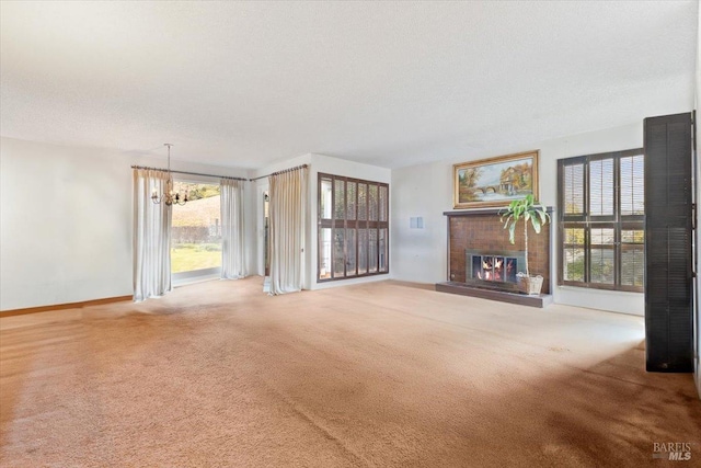 unfurnished living room featuring a chandelier, a textured ceiling, carpet floors, and a brick fireplace