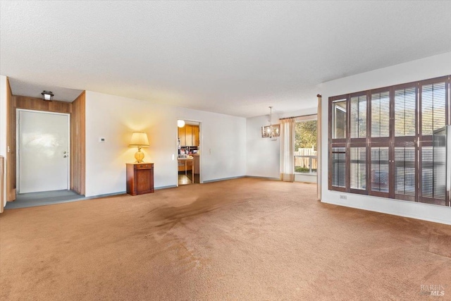 unfurnished living room featuring a textured ceiling, carpet floors, an inviting chandelier, and wood walls