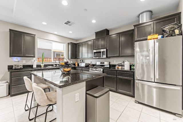 kitchen featuring appliances with stainless steel finishes, a breakfast bar, dark stone countertops, a center island, and light tile patterned floors