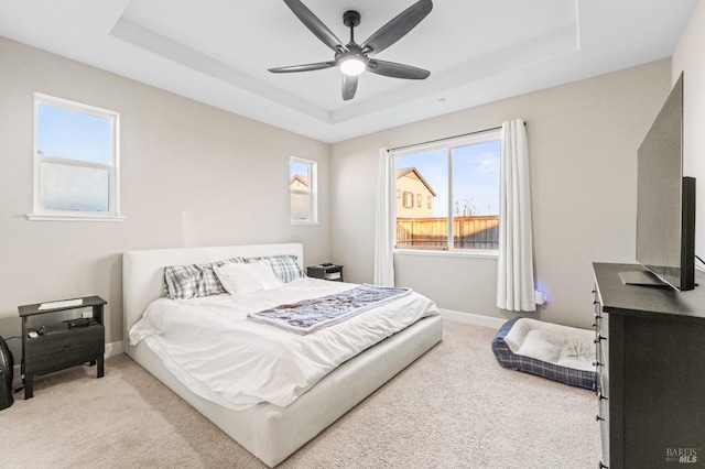 bedroom with a raised ceiling, light carpet, and ceiling fan