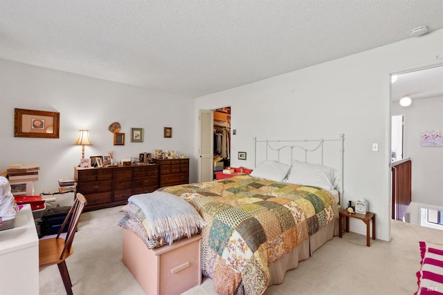 bedroom with a spacious closet, a textured ceiling, light carpet, and a closet