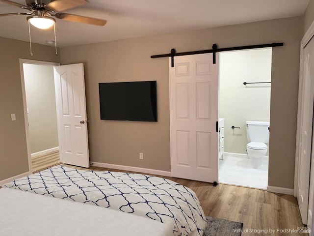 unfurnished bedroom featuring ceiling fan, connected bathroom, a barn door, and light hardwood / wood-style floors