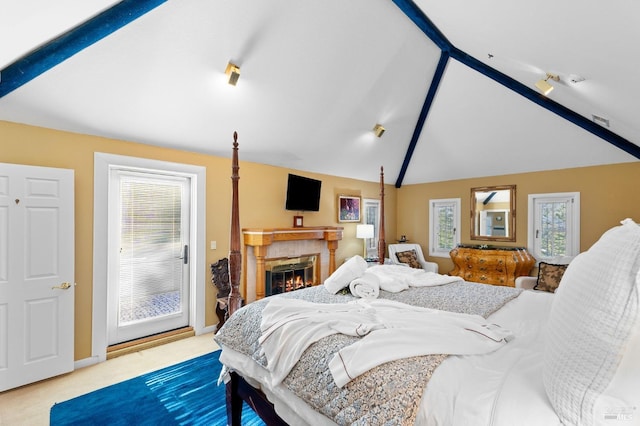 carpeted bedroom featuring vaulted ceiling with beams, a fireplace, multiple windows, and access to exterior