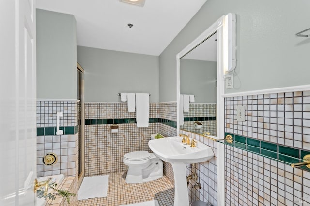 bathroom with toilet, tile patterned floors, and tile walls