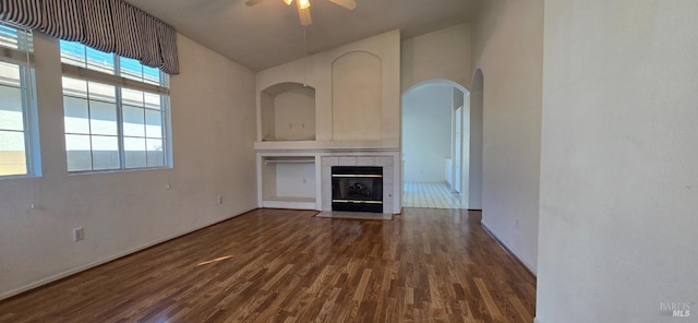 unfurnished living room featuring ceiling fan, a towering ceiling, dark wood-type flooring, and a tiled fireplace