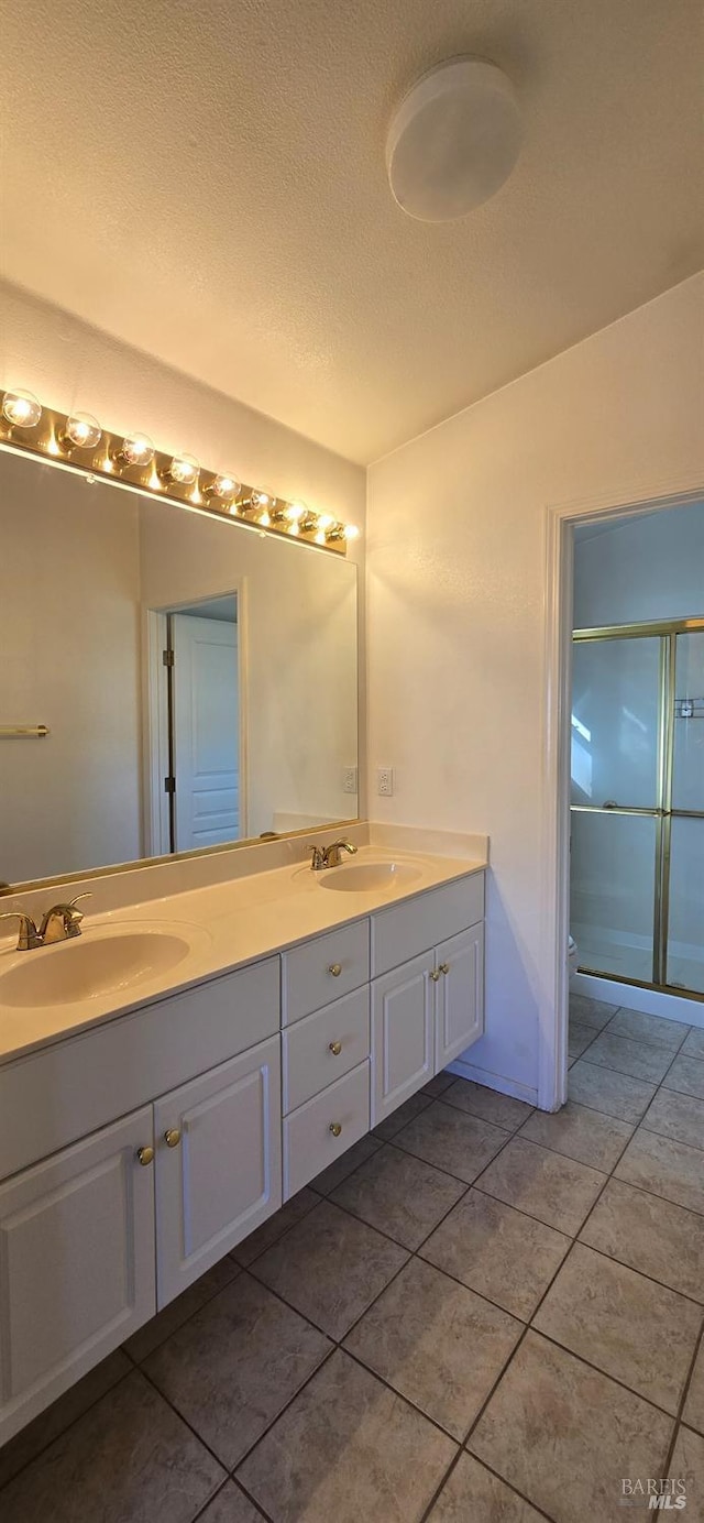 bathroom featuring a textured ceiling, vanity, tile patterned floors, and a shower with shower door