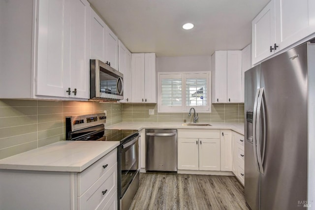 kitchen with white cabinets, stainless steel appliances, a sink, and light countertops