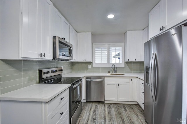 kitchen featuring tasteful backsplash, light wood-style flooring, appliances with stainless steel finishes, white cabinetry, and a sink