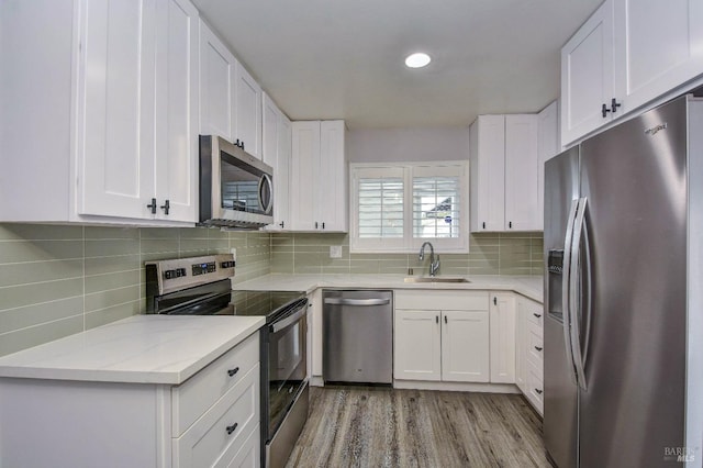 kitchen featuring stainless steel appliances, a sink, white cabinets, light wood-type flooring, and backsplash