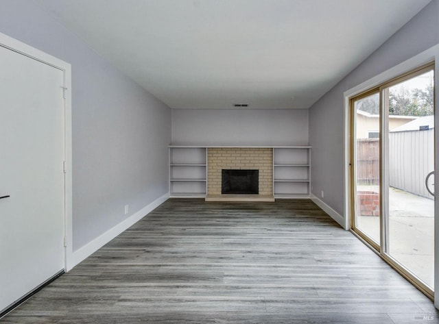 unfurnished living room featuring visible vents, a fireplace, baseboards, and wood finished floors