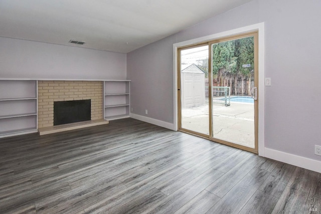 unfurnished living room featuring a brick fireplace, visible vents, baseboards, and wood finished floors