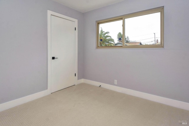 spare room featuring light carpet and baseboards