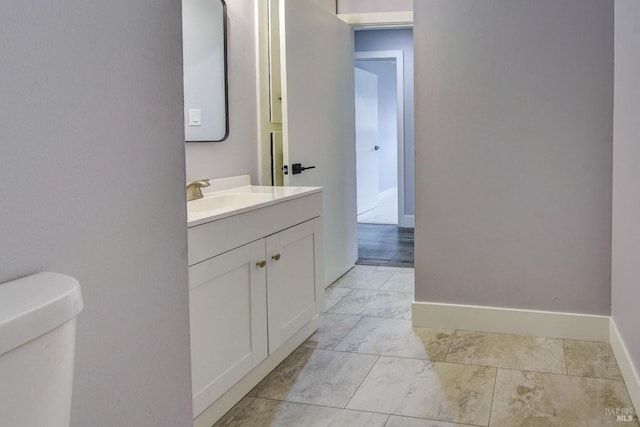 bathroom with toilet, marble finish floor, vanity, and baseboards