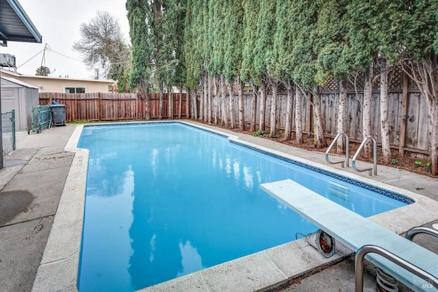 view of swimming pool featuring a fenced in pool, a storage unit, a fenced backyard, an outdoor structure, and a diving board